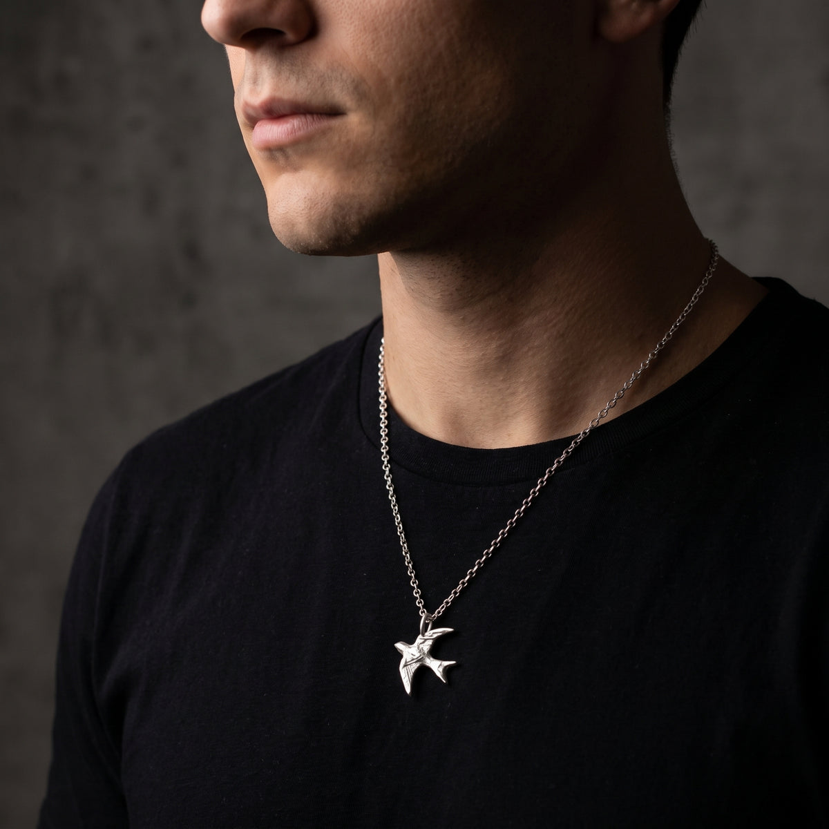 Side-profile view of a man wearing the textured silver swallow pendant over a black T-shirt.