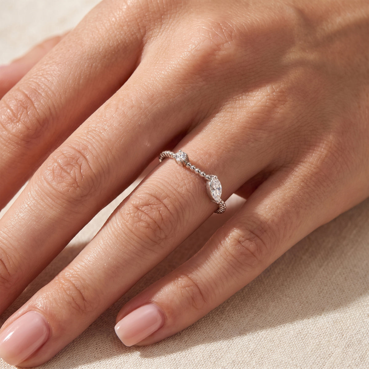 Close-up of the silver beaded bypass ring with clear marquise and round stones worn on a finger.