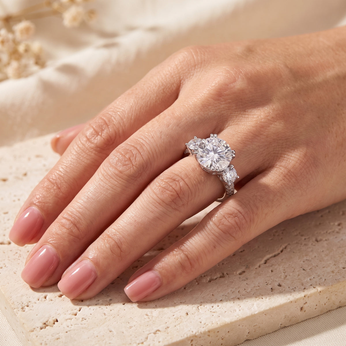 Top view of the silver three-stone ring worn on a hand resting on a stone block.