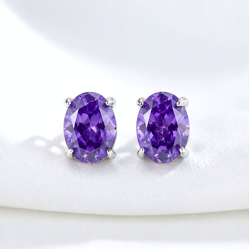 Front view of oval cut purple simulated amethyst stud earrings in silver settings on white fabric.