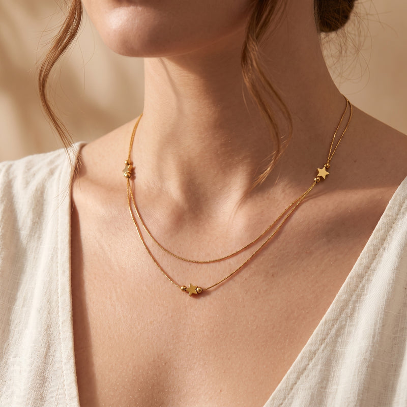 Model wearing a gold-tone double-strand necklace with star stations over a white blouse.