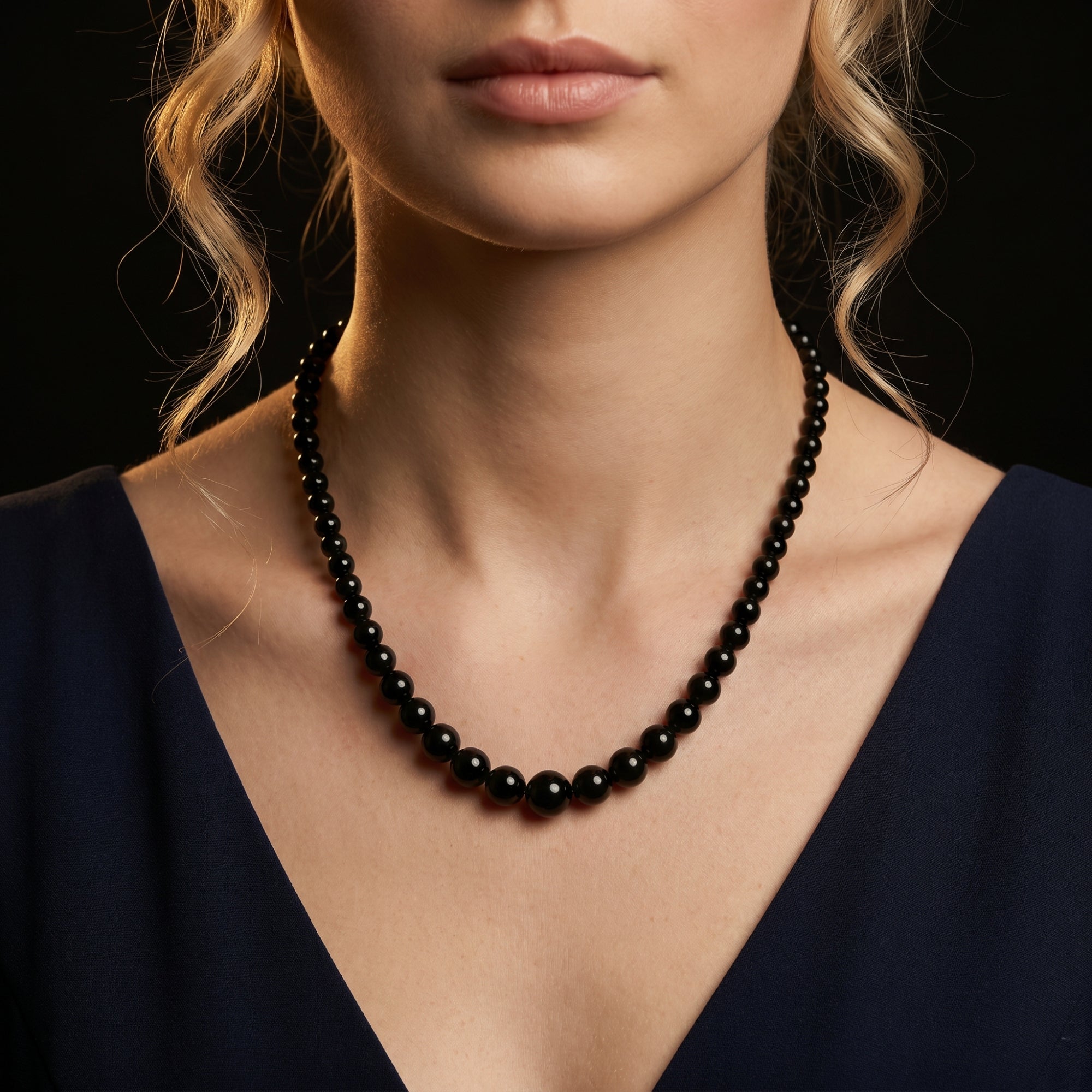 Model wearing the Penumbra graduated natural black onyx bead necklace with silver hardware against a dark background.