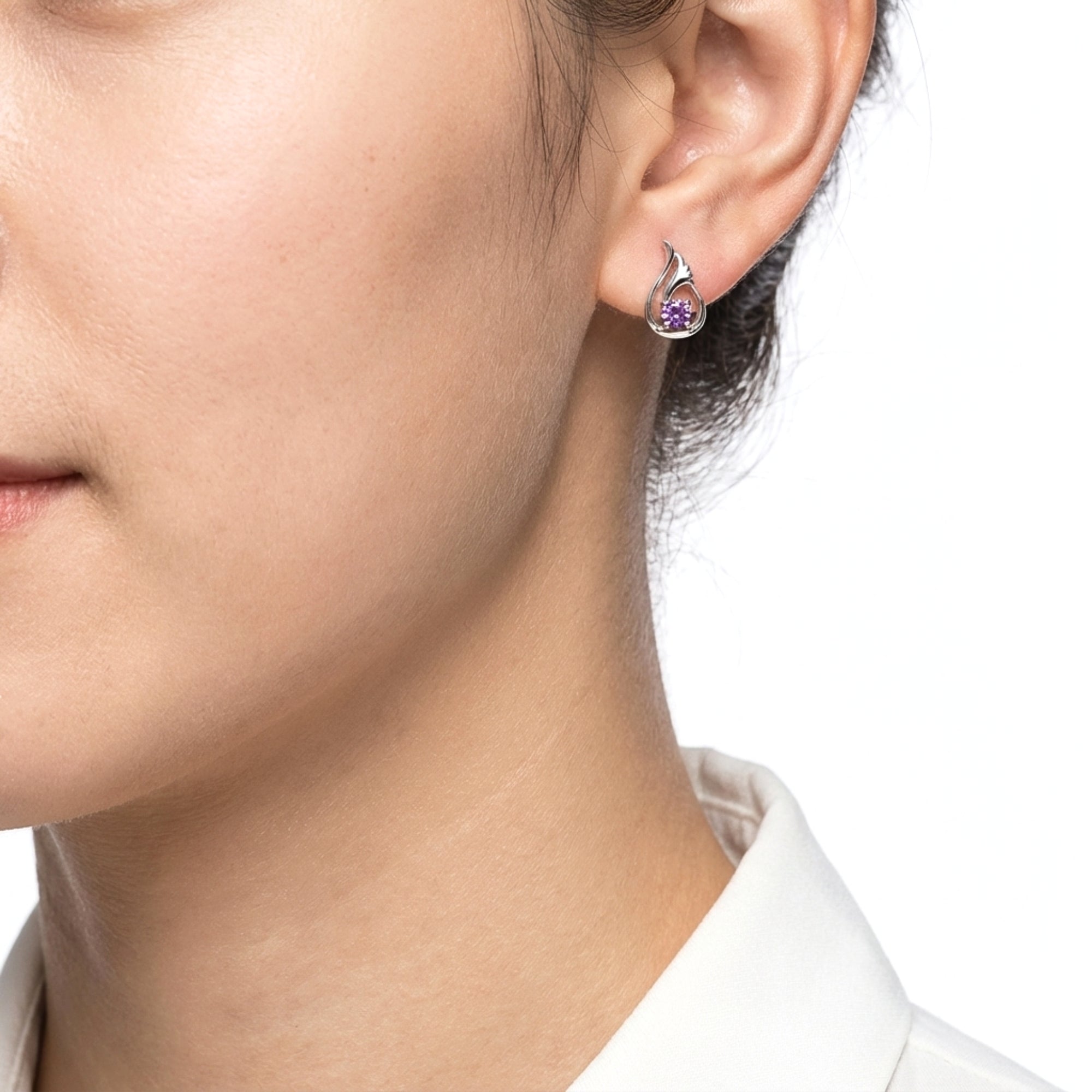 Close-up of a sterling silver Lysithea drop earring with a round simulated amethyst stone worn on a model's ear.