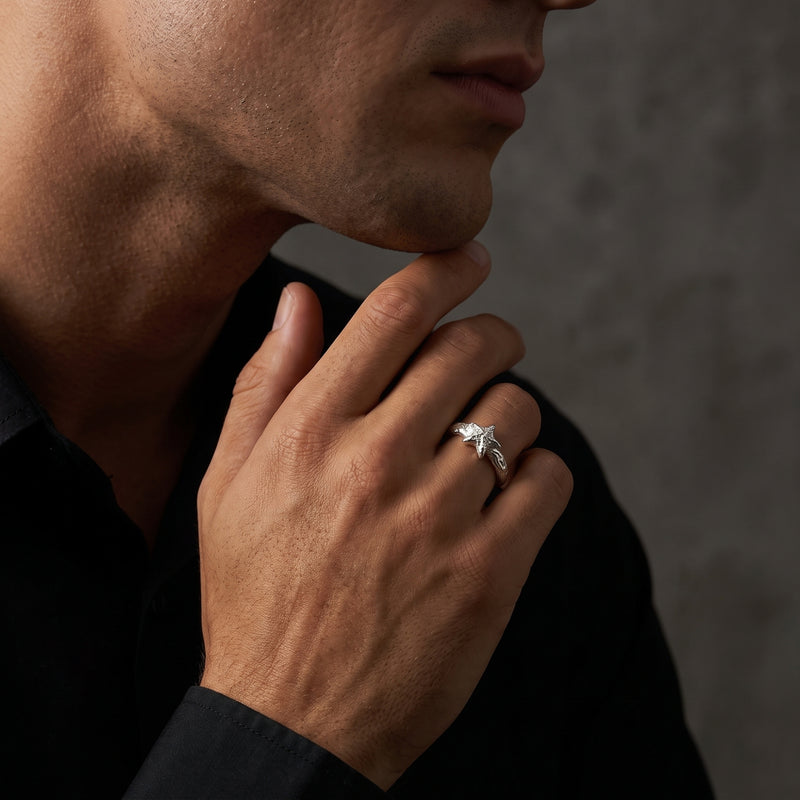 Man wearing a textured silver star ring on his finger with his hand resting at his chin.