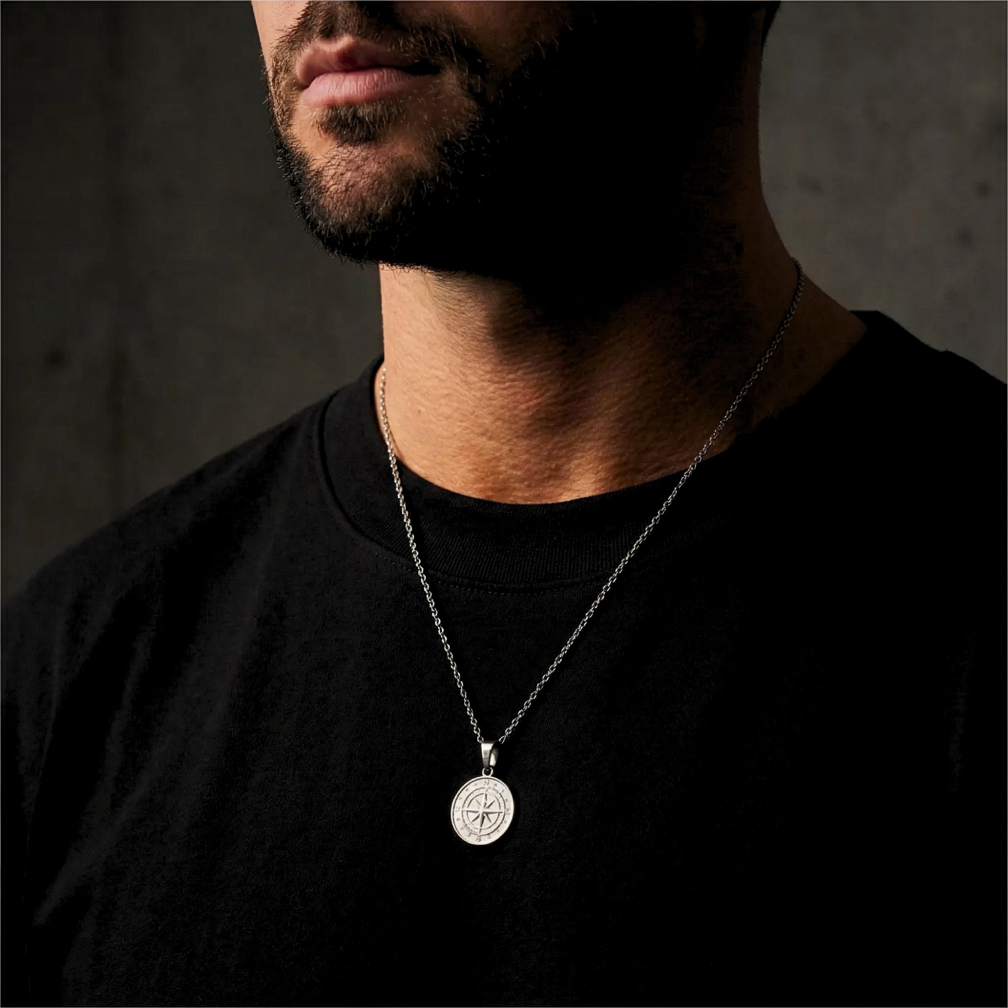 Men's silver stainless steel compass pendant necklace worn by a model over a black t-shirt.