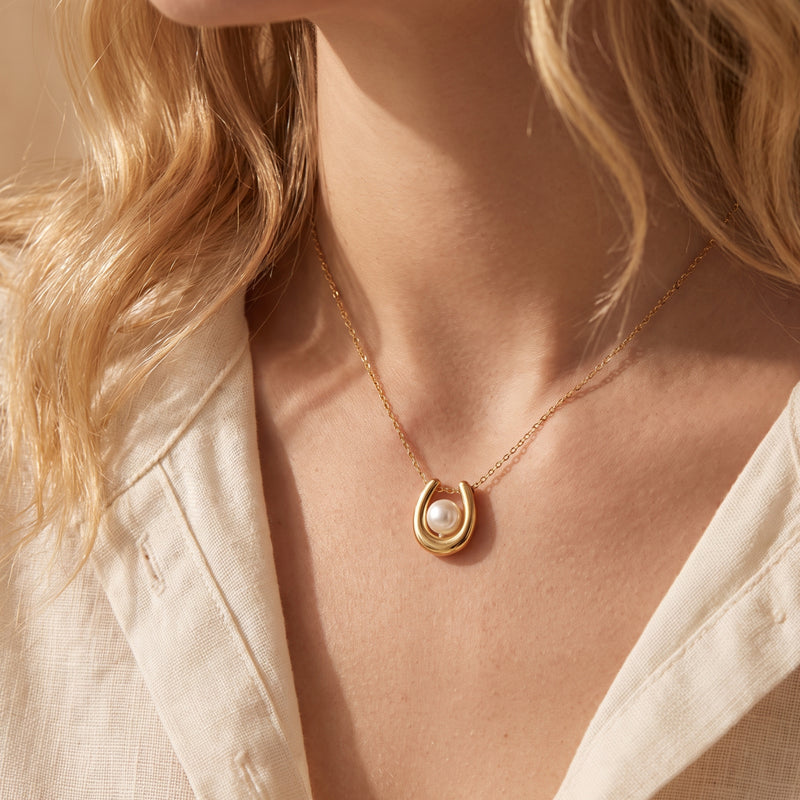 Close-up of a model wearing the gold-tone horseshoe necklace with a centered white pearl.