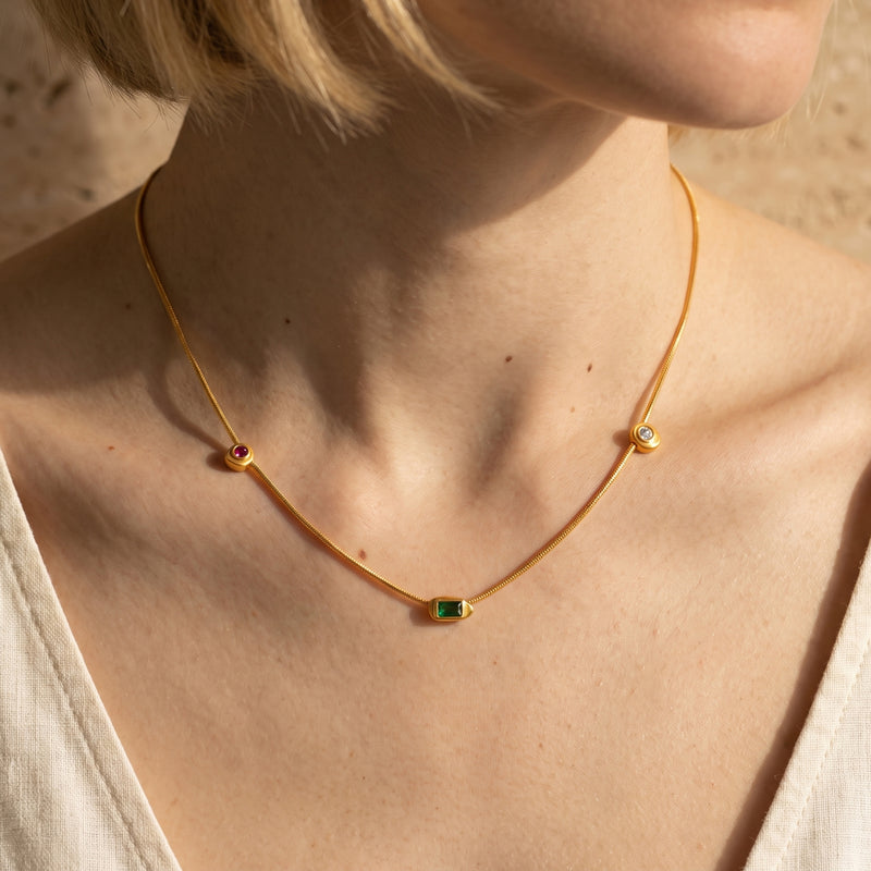 Front on-model view of the gold station necklace with a green center stone and red and clear side stations.