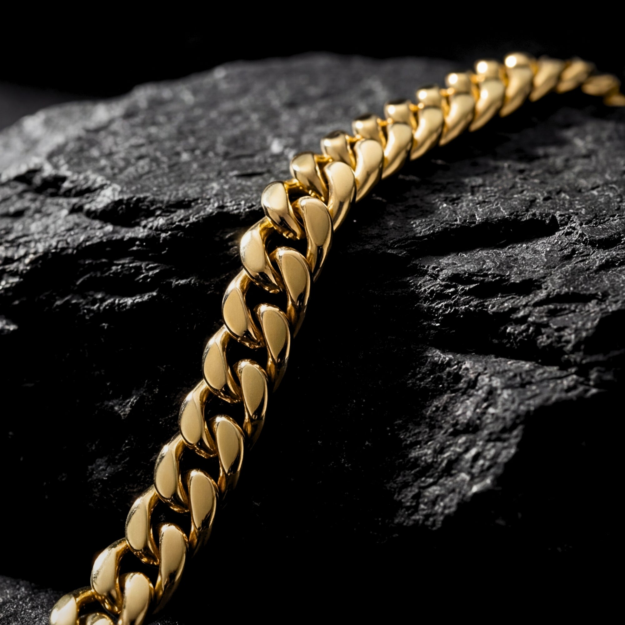 Macro detail shot of the polished gold stainless steel links of the Cuban bracelet on a dark rock.