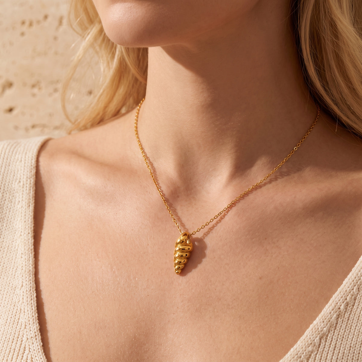 Front view of a model wearing the gold-tone spiral shell pendant necklace with a cream V-neck top.