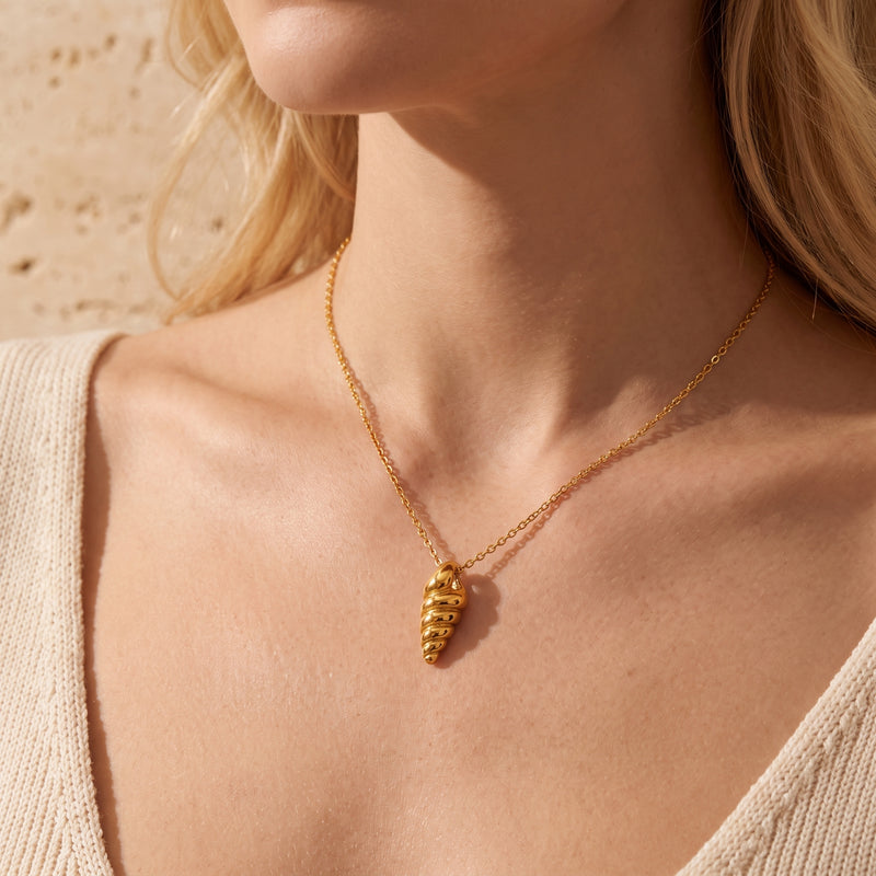 Front view of a model wearing the gold-tone spiral shell pendant necklace with a cream V-neck top.