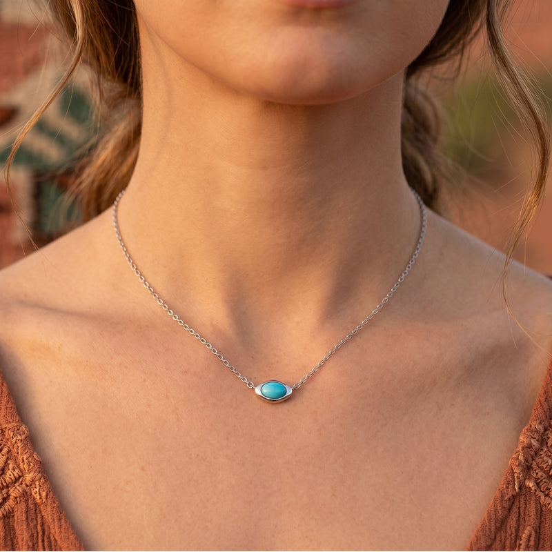 Woman wearing the silver turquoise necklace with a horizontal cabochon pendant against a soft desert background.