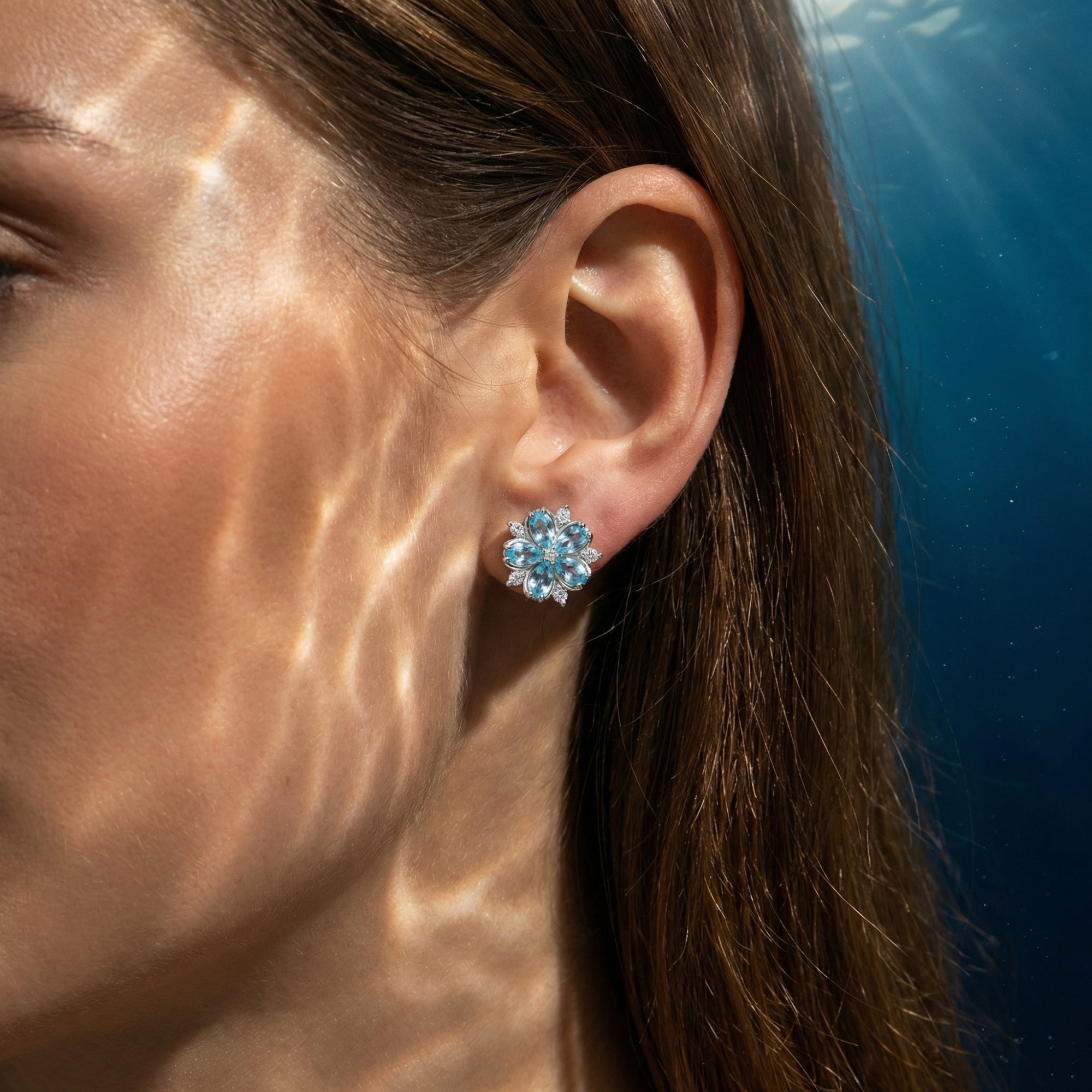 A woman wearing a marquise-cut aquamarine flower stud earring in sterling silver.