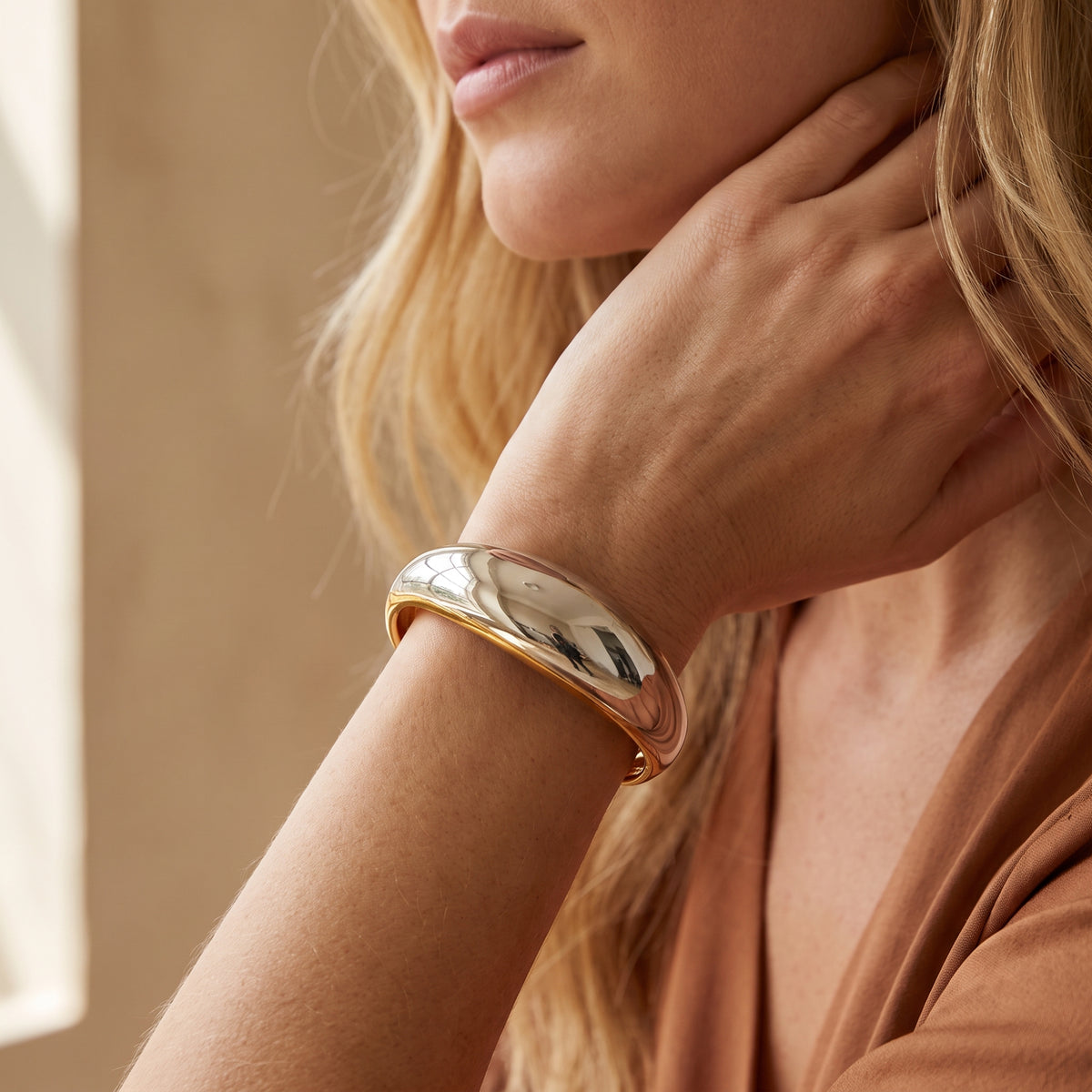 Model wearing the Sculpted Dome Bracelet on her wrist, showing its smooth gold- and silver-tone design.