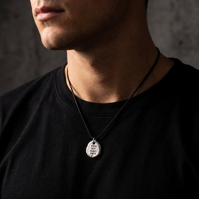 Man wearing the engraved silver pebble pendant on a black cord over a black shirt.