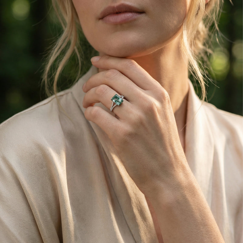 Model wearing a cushion cut moss agate sterling silver ring on her finger in a natural outdoor setting.