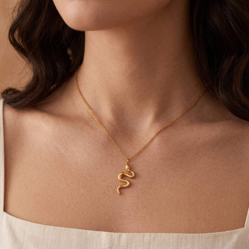 Close-up of a person wearing the gold-tone serpent pendant necklace centered on the upper chest.