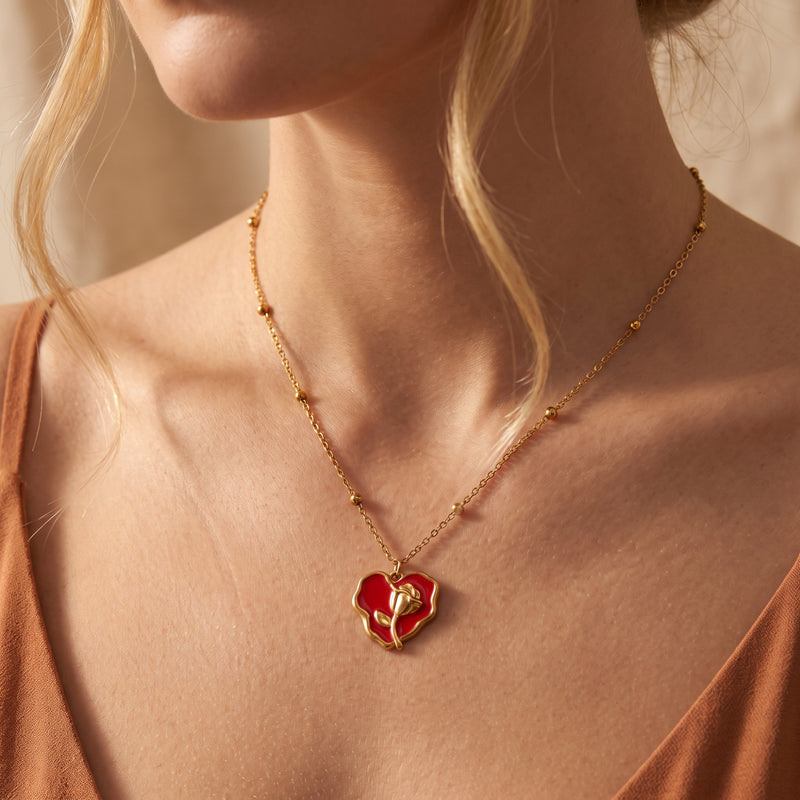 Model wearing the red enamel rose heart pendant necklace with a gold-tone beaded chain and rust-colored top.