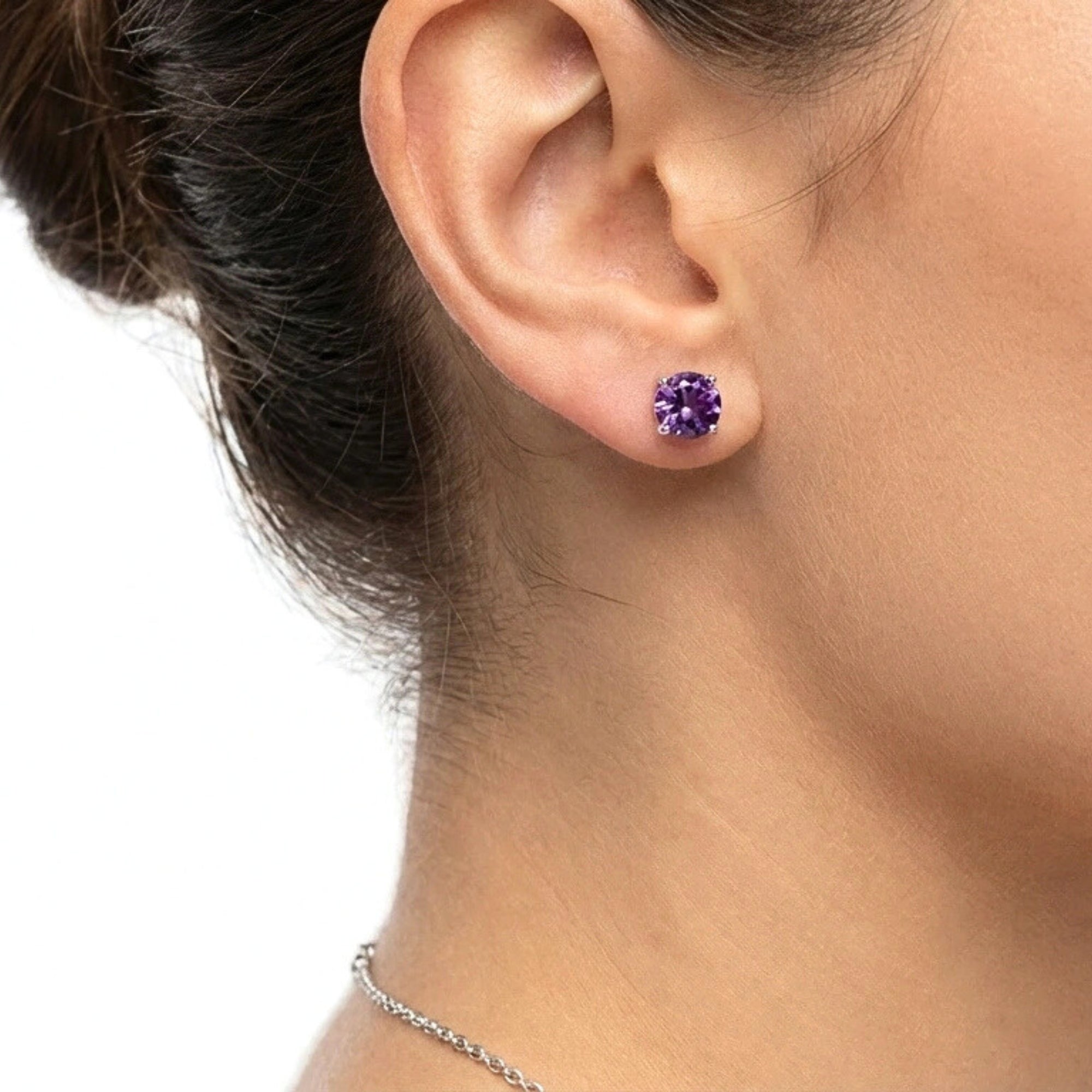 Close-up of a woman wearing a round cut simulated amethyst stud earring in sterling silver.