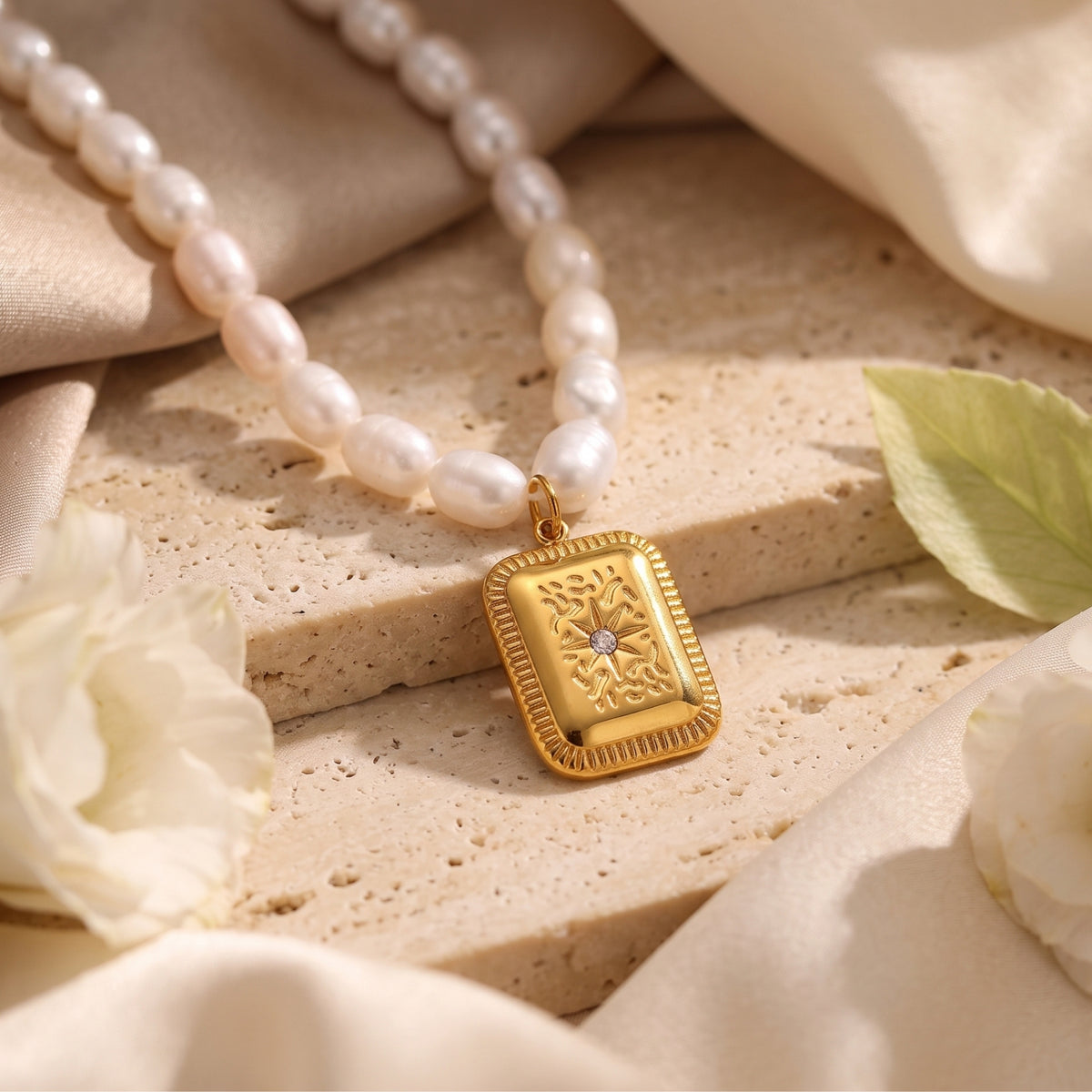 Close-up of the rectangular gold-tone starburst pendant hanging from a freshwater pearl strand.
