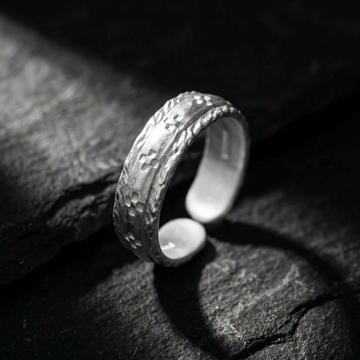Angled view of the etched silver open band ring standing on dark stone, showing its adjustable gap.