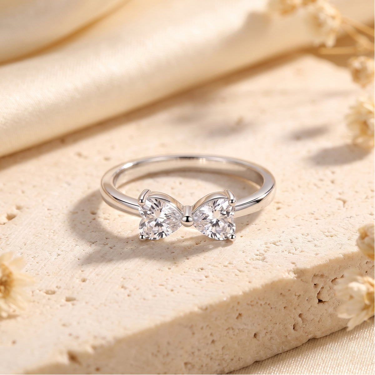 Front view of the silver ring with twin heart-cut clear zircons forming a bow motif on a stone slab.