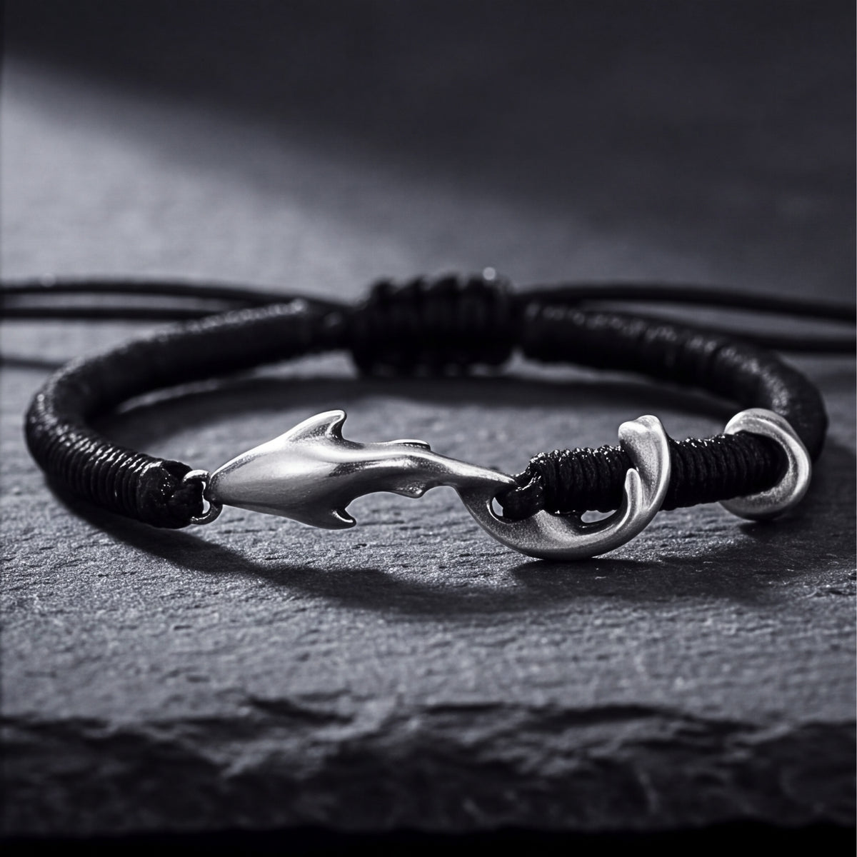 Close-up front view of the black cord bracelet featuring a silver dolphin hook clasp on dark stone.
