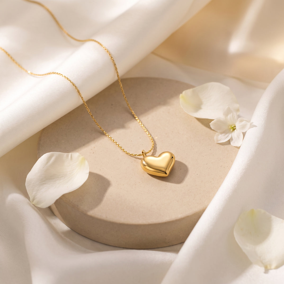 Gold-tone puffed heart necklace arranged on a round beige display plate among white flower petals.