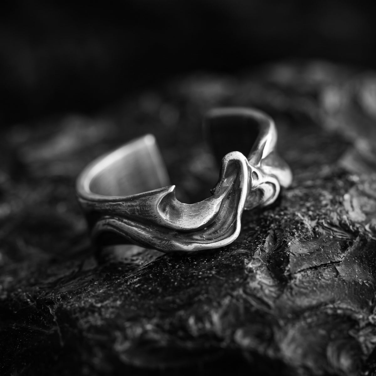Angled close-up of the sculpted silver wave open ring resting on jagged dark rock.