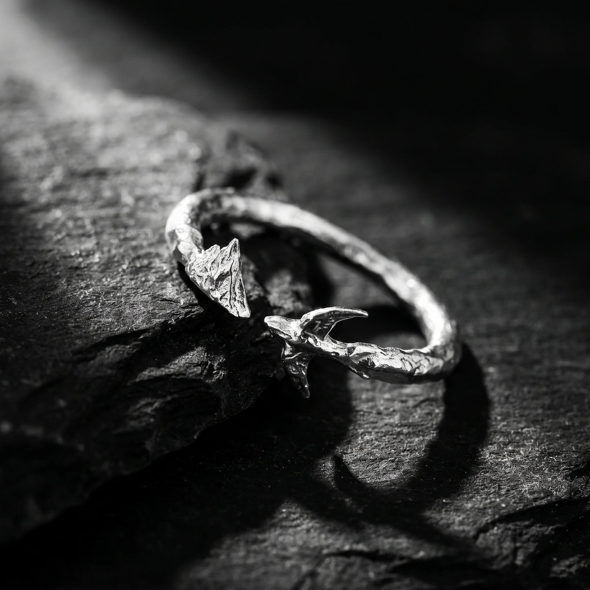 Angled close-up of the textured silver open-band ring with mountain and bird details on a dark stone surface.