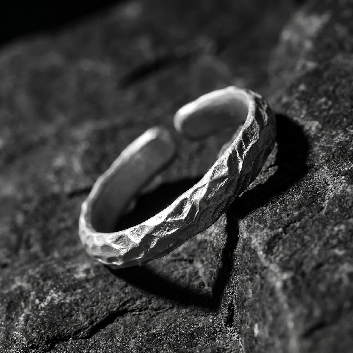 Angled top-down view of the textured silver open-band ring resting on dark rock, showing its gap.