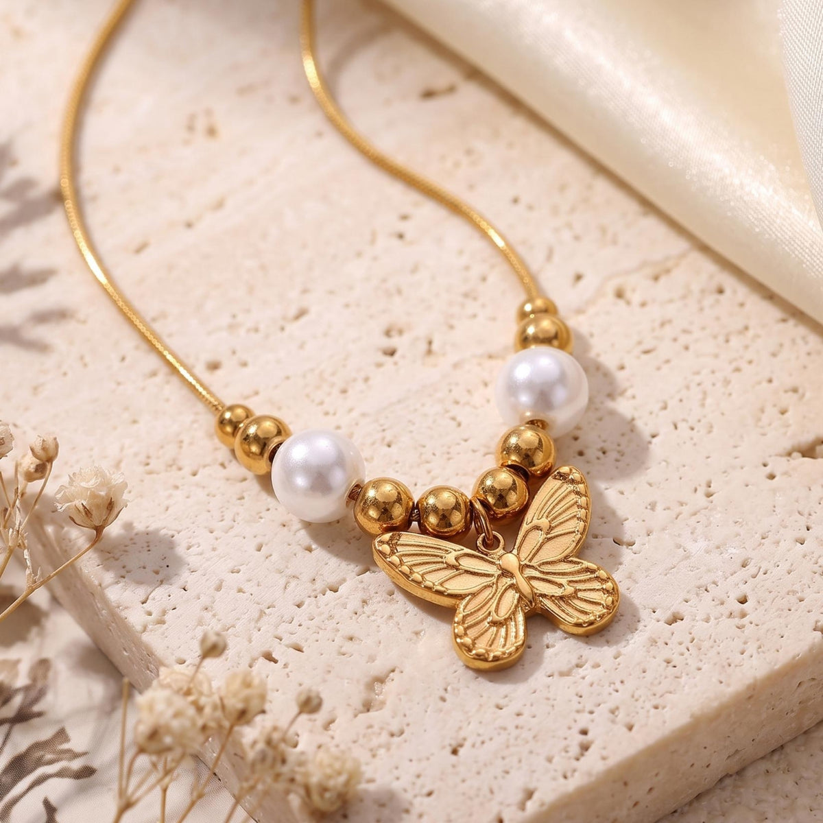 Close-up of a gold-tone etched butterfly pendant with white pearls and gold beads on a textured stone surface.