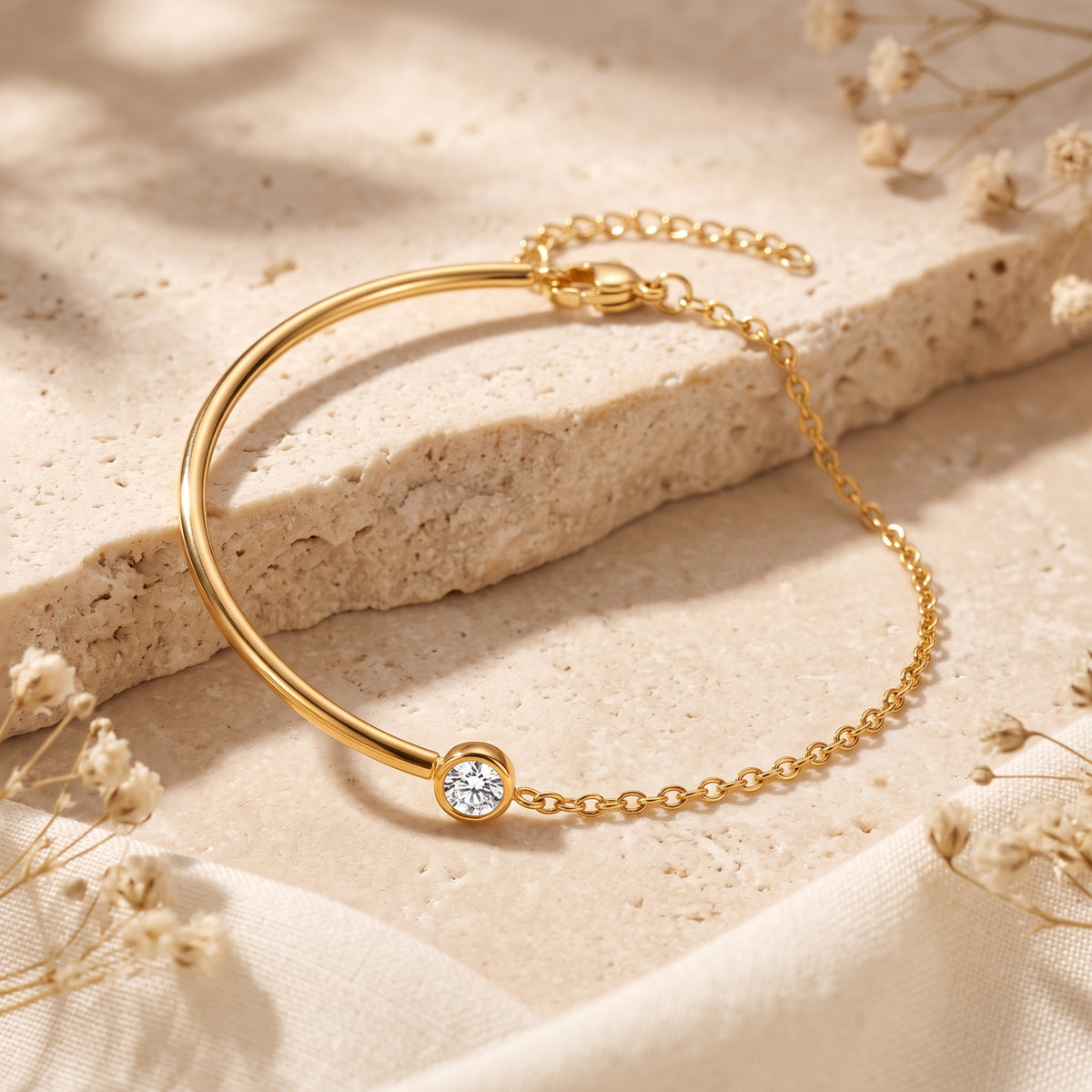 Angled overhead view of the gold-tone bezel station cuff bracelet resting on a beige textured stone slab.