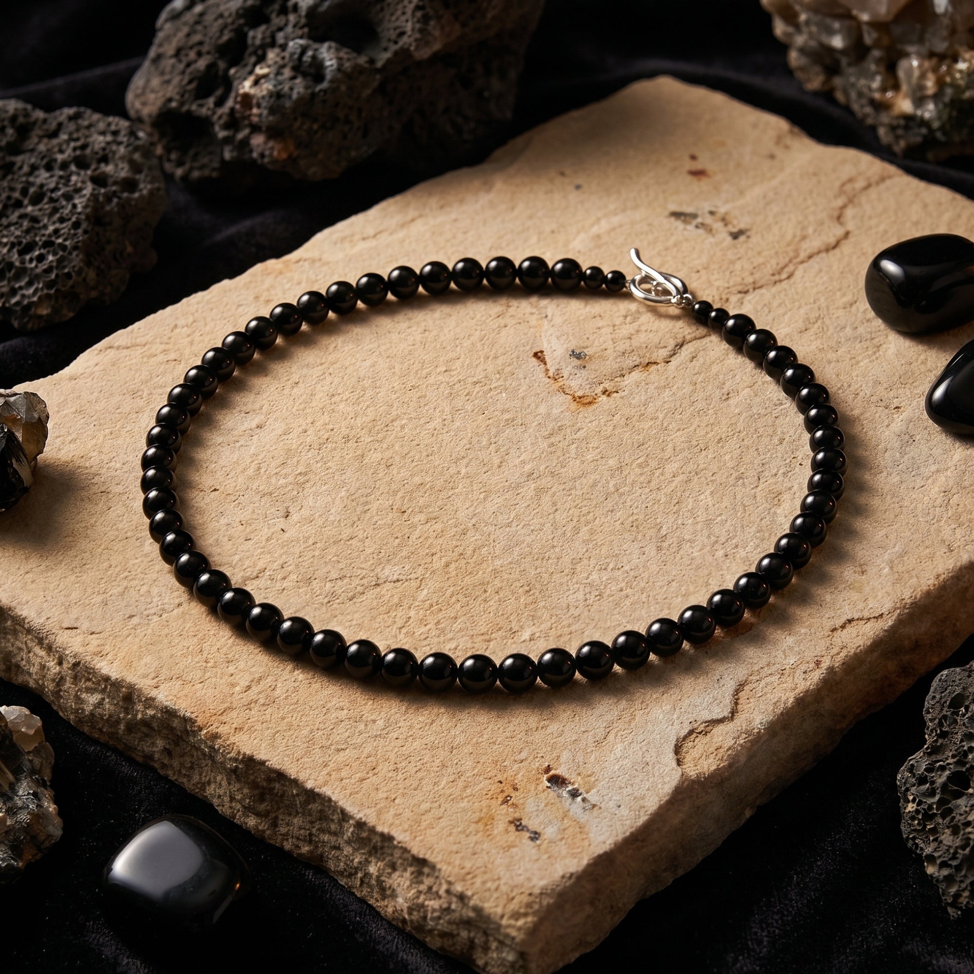 Angled view of the 6mm round black onyx beaded necklace with sterling silver clasp on a stone surface.