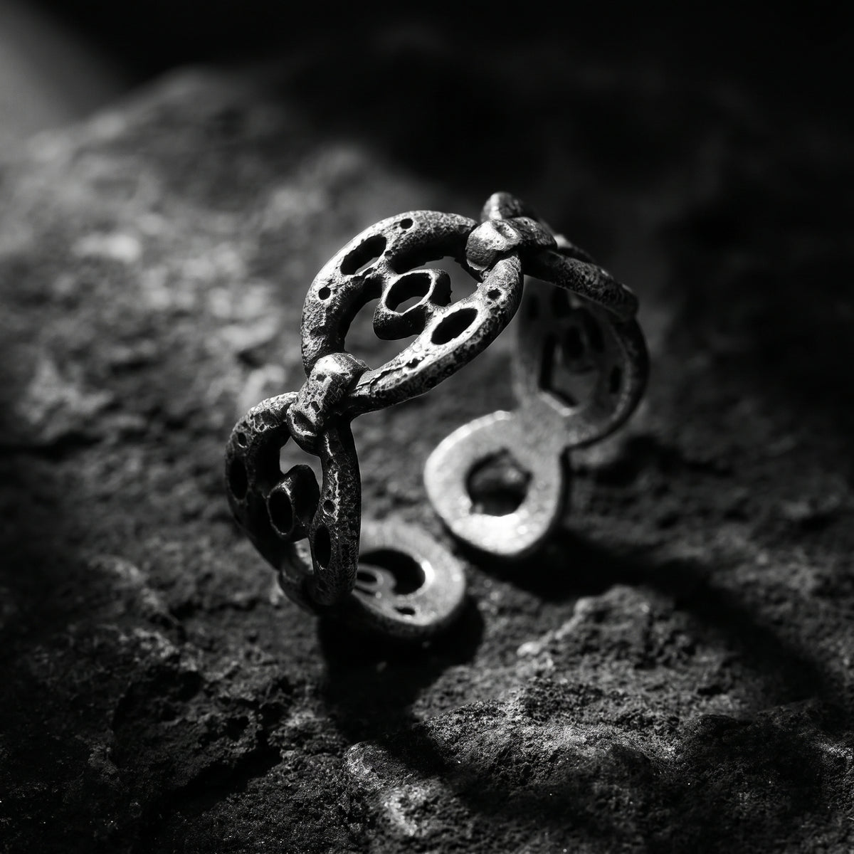 Angled macro view of the distressed silver oval-link ring on textured rock, showing the open band.