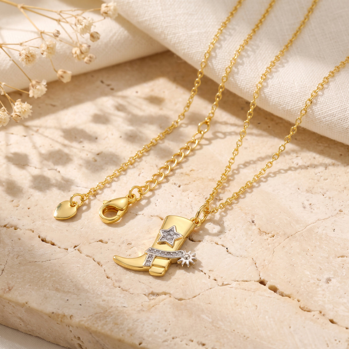 Flat lay of the boot pendant necklace with chain, lobster clasp, extender links, star, and spur details.