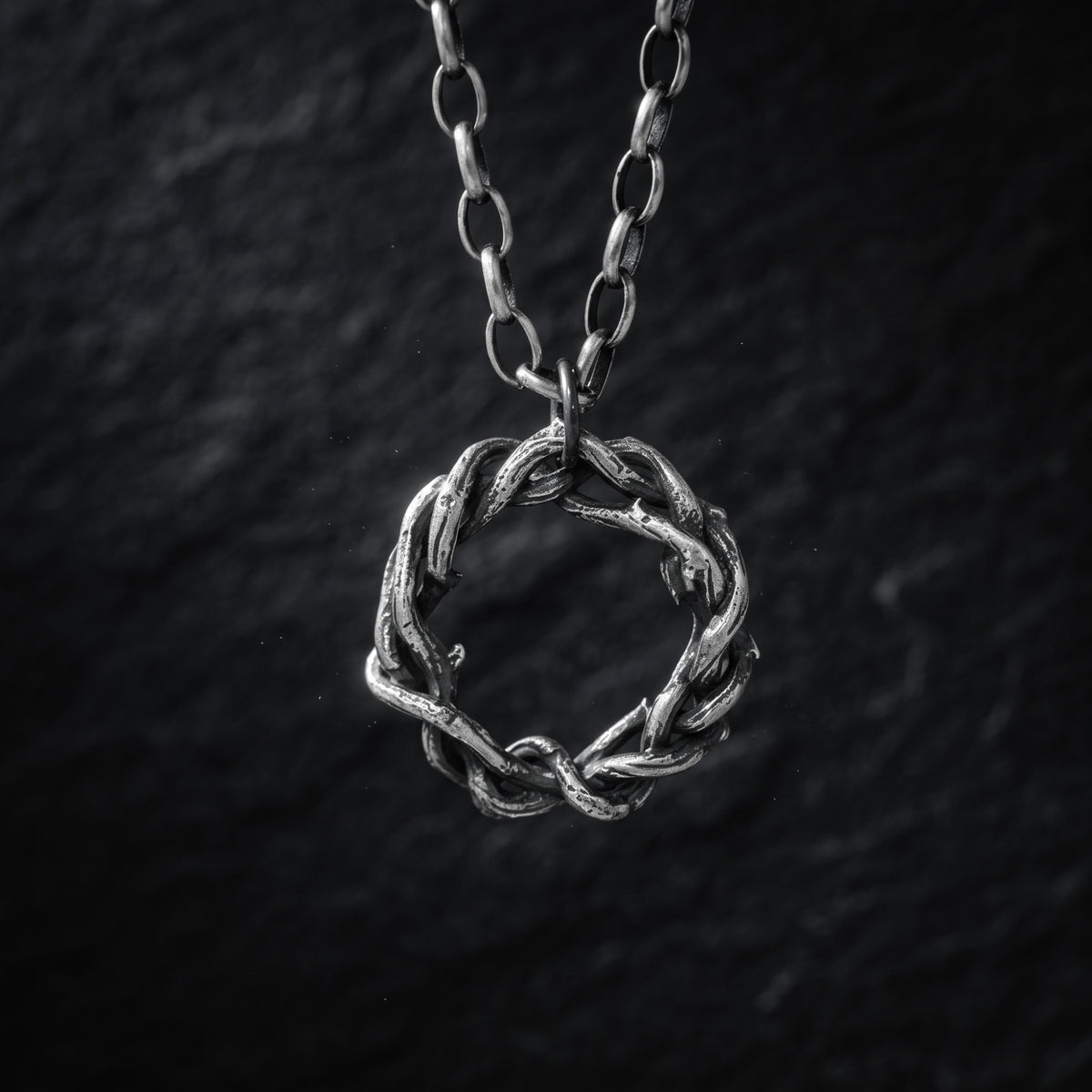 Close-up of the silver intertwined circular pendant hanging from its chain against a dark textured backdrop.