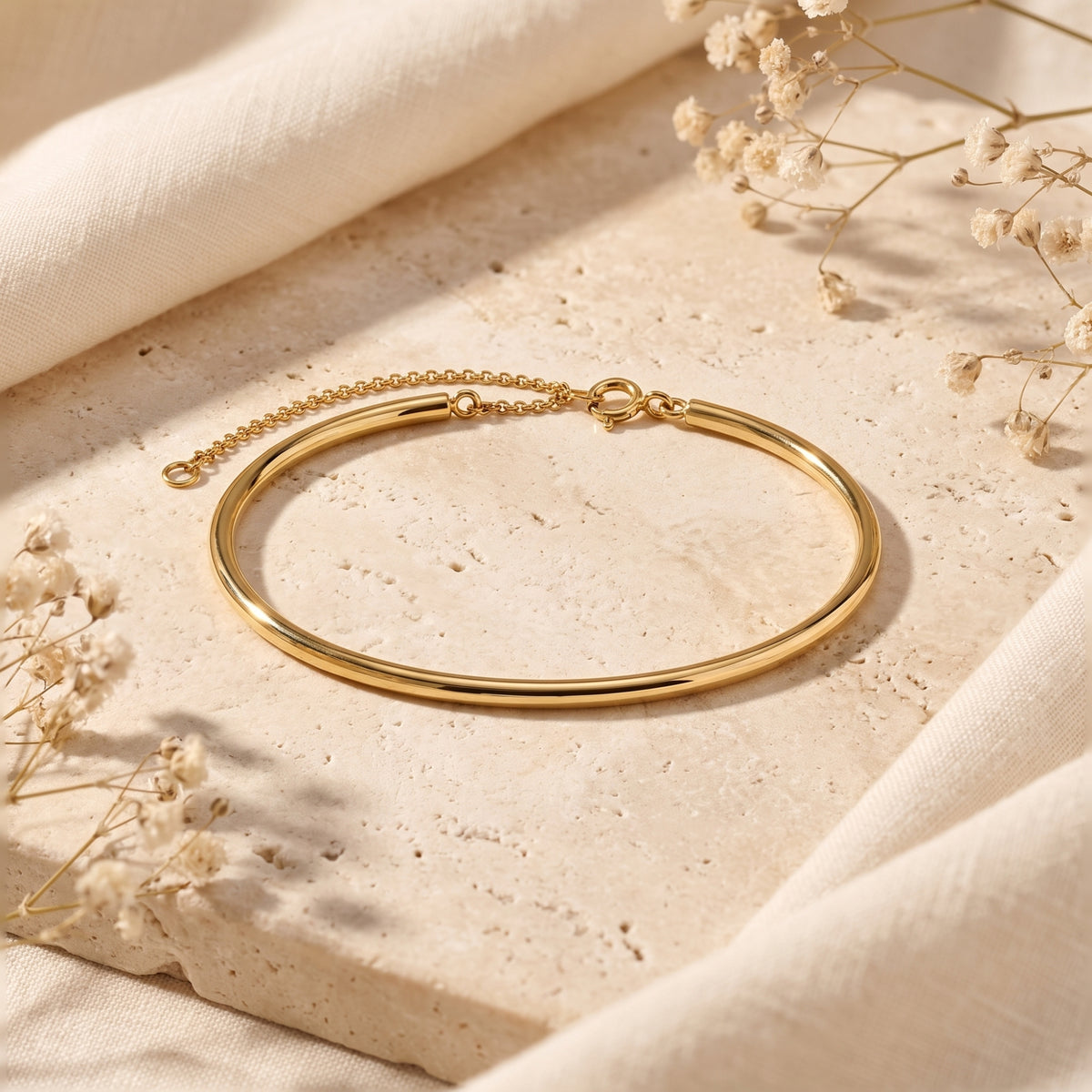 Gold-toned arc half-bangle bracelet displayed flat on a beige stone surface with its clasp and chain visible.