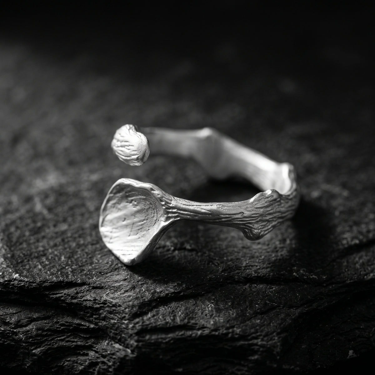Angled view of the silver open ring on dark rock, showing its bark-inspired texture and open gap.