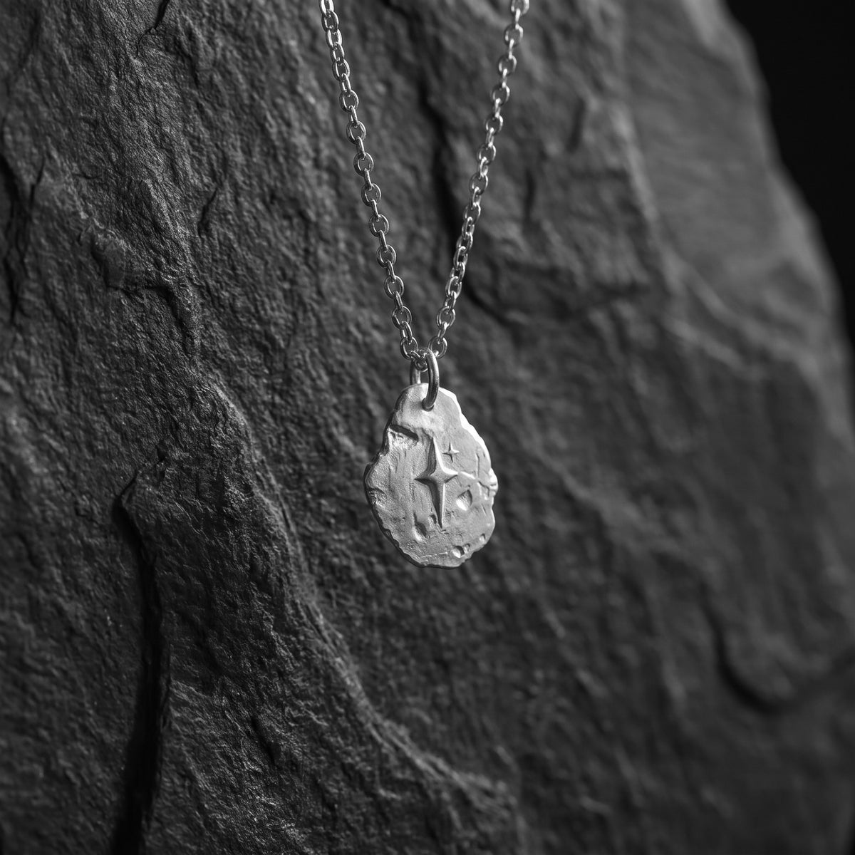 Silver starburst pendant hanging vertically from its chain against dark slate.