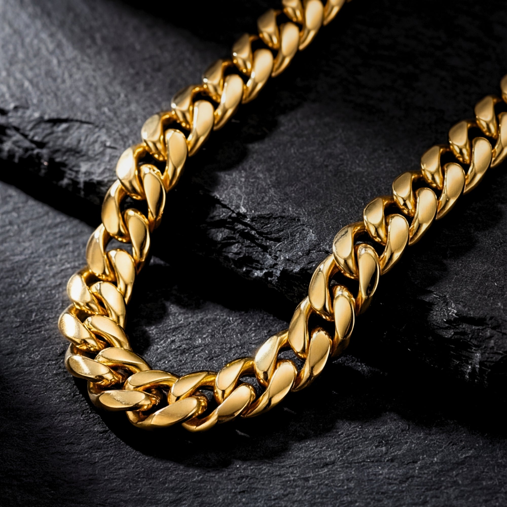 Angled close-up of the 12mm gold-tone stainless steel Cuban links on a dark stone background.