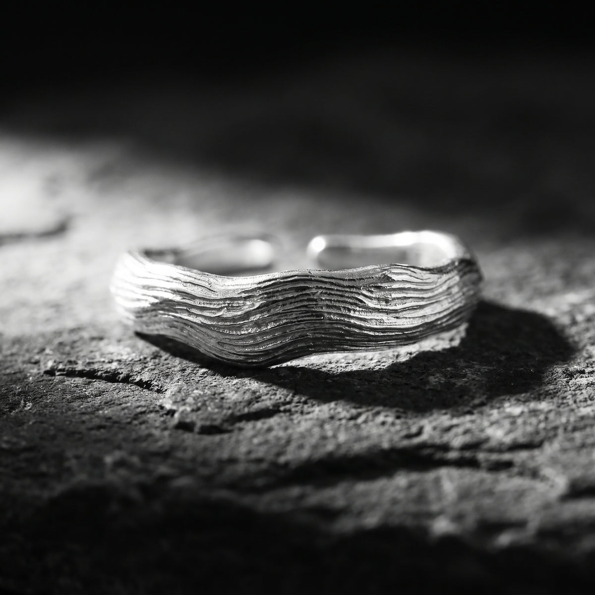 Horizontal close-up of the silver open-band ring showing carved wave ridges on dark slate.