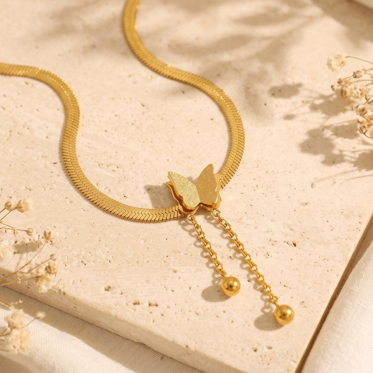 Overhead view of the gold-tone butterfly tassel necklace displayed flat on a textured beige stone slab.