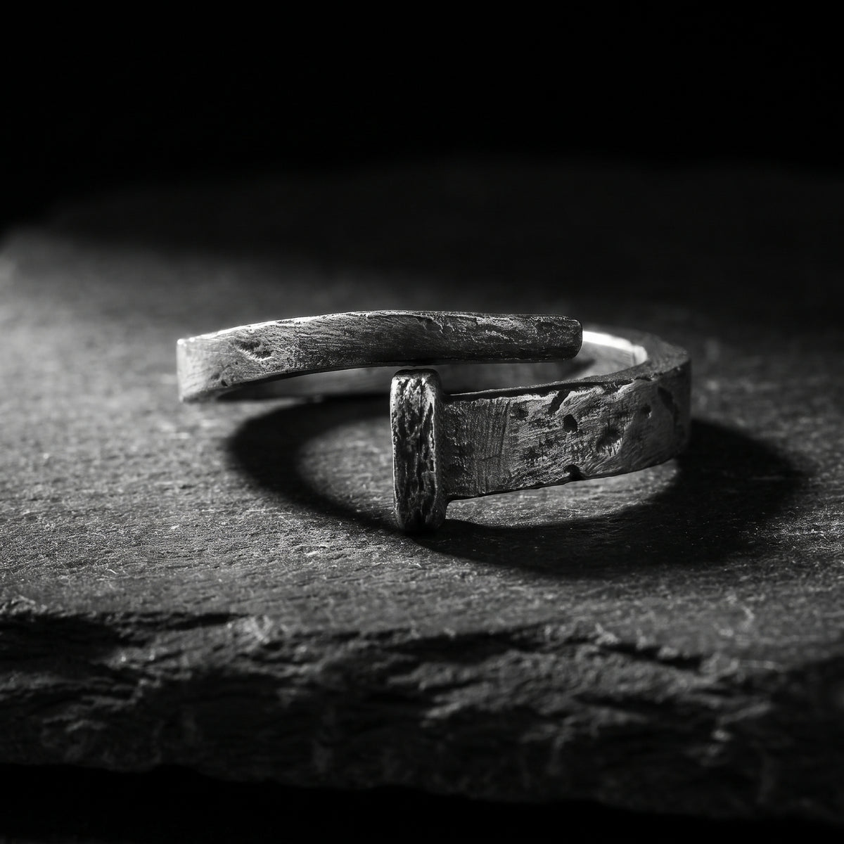 Side view of the textured silver nail-style open-band ring displaying its open ends on a dark textured surface.