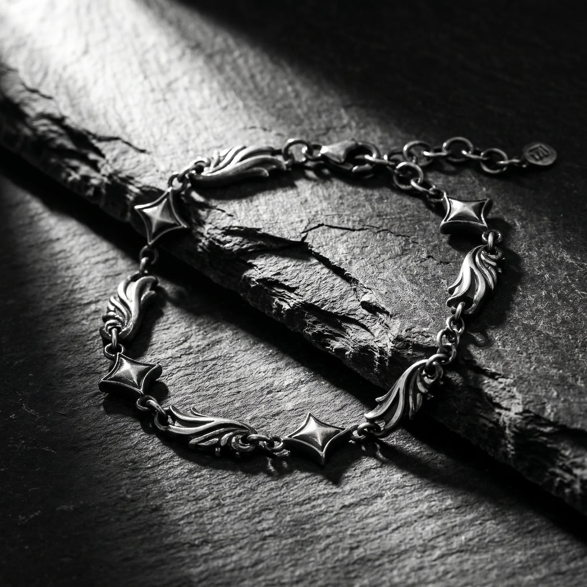 Close-up of the silver star and scroll link bracelet on textured slate, with its extension chain and tag visible.