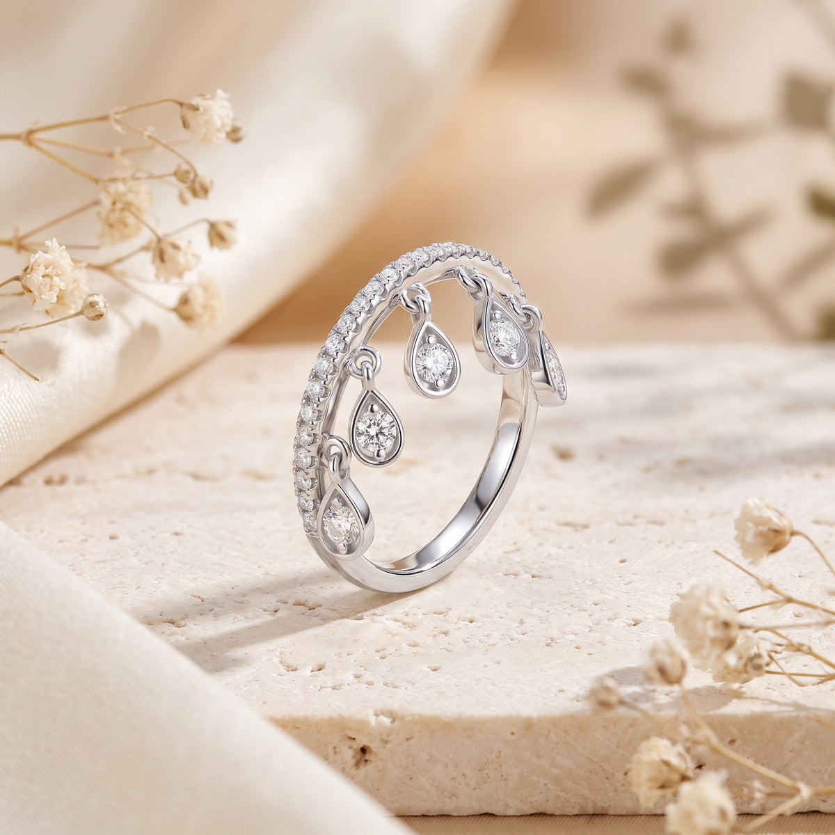Angled view of a silver pavé band ring standing upright with five hanging teardrop stone charms.