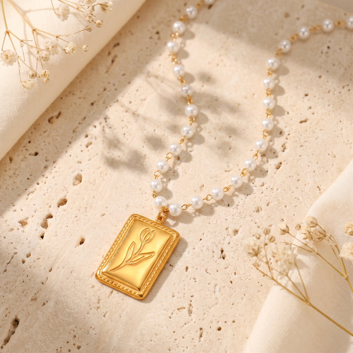 Angled view of the gold-tone tulip tag pendant resting on textured beige stone with a white pearl strand.