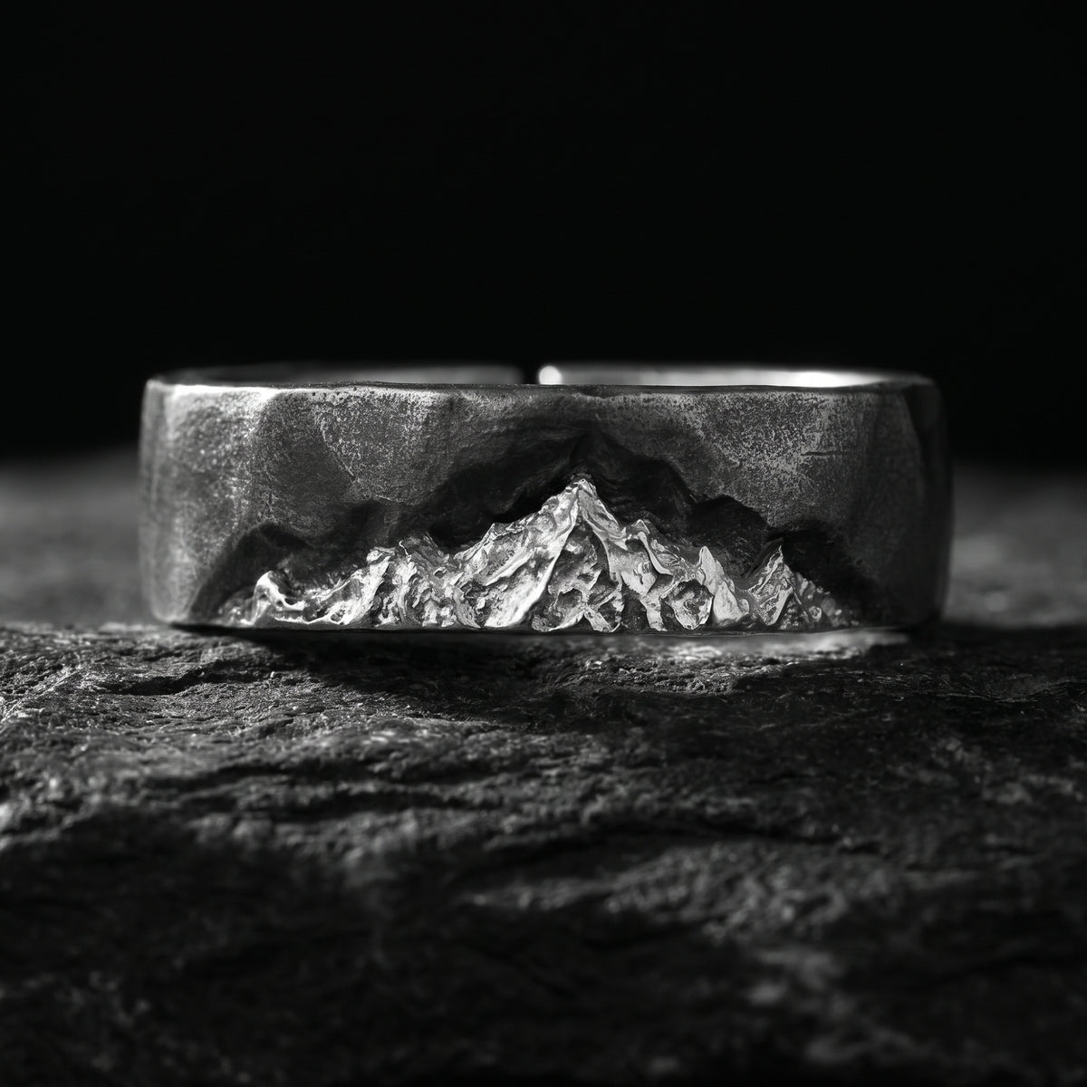 Frontal macro view of the silver open ring on dark rock, highlighting its carved mountain range.