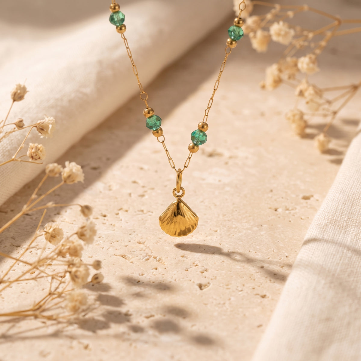 Close-up of the gold-tone shell pendant hanging from a green-beaded chain above a textured stone surface.