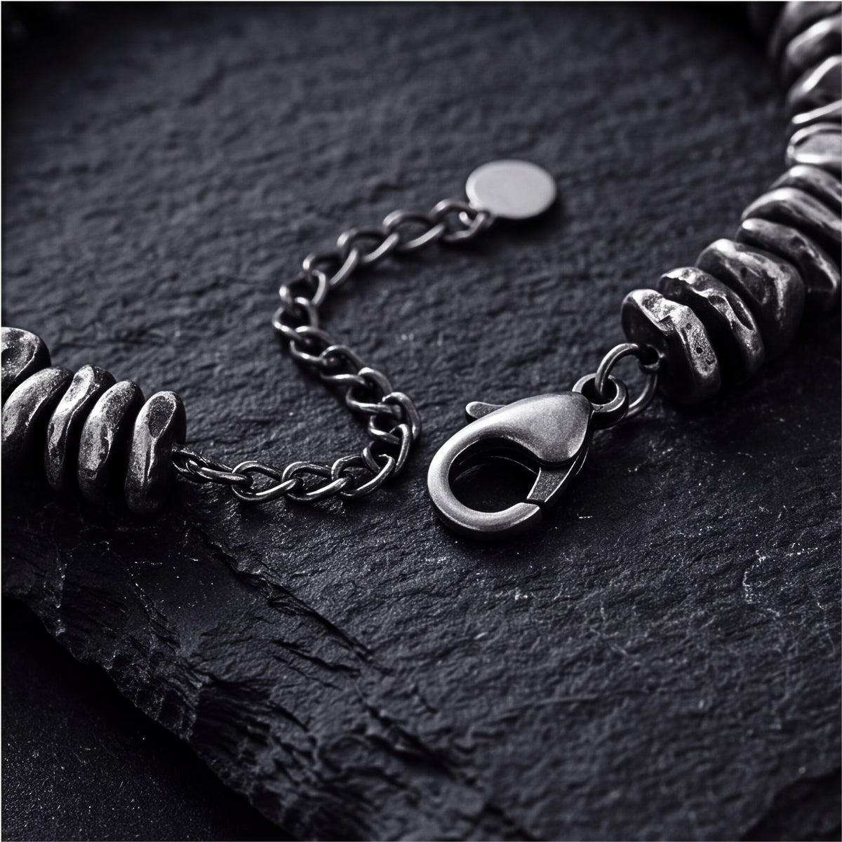 Macro view of the silver pebble link bracelet’s lobster clasp and extension chain on textured dark slate.