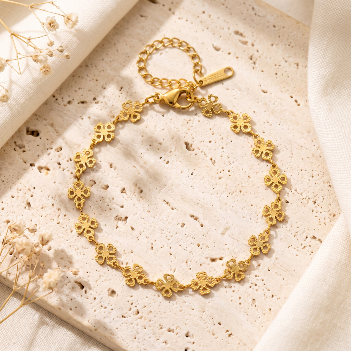 Full flat lay of the gold-tone four-leaf clover bracelet on stone, with lobster clasp and extender chain visible.